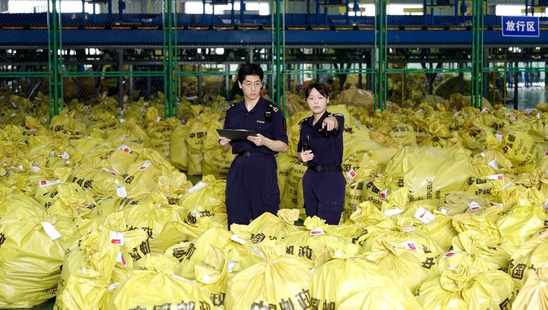 海关关员在跨境电商货物仓库内查验,两名关员手持单据核对成堆待出口包裹